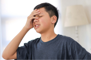Child with a headache at a school desk, illustrating migraines when school starts