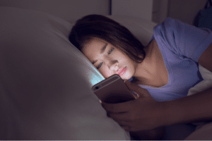 Teenager in bed at night looking at a phone, illustrating the link between screen time and sleep